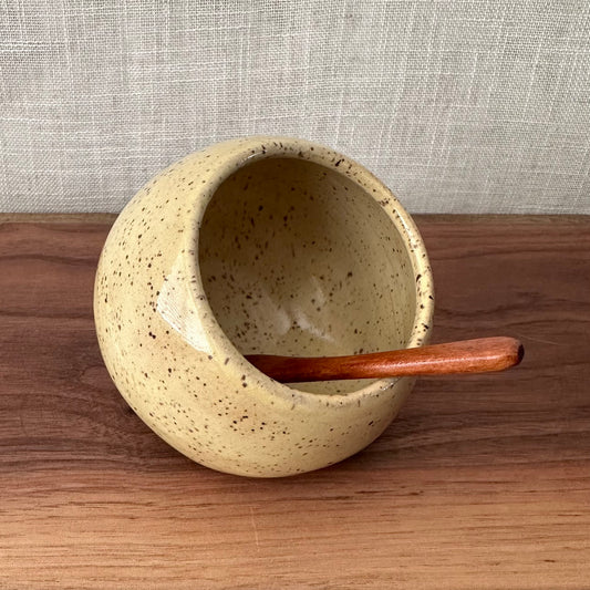 Speckled ceramic bowl with a wooden spoon on a wooden surface