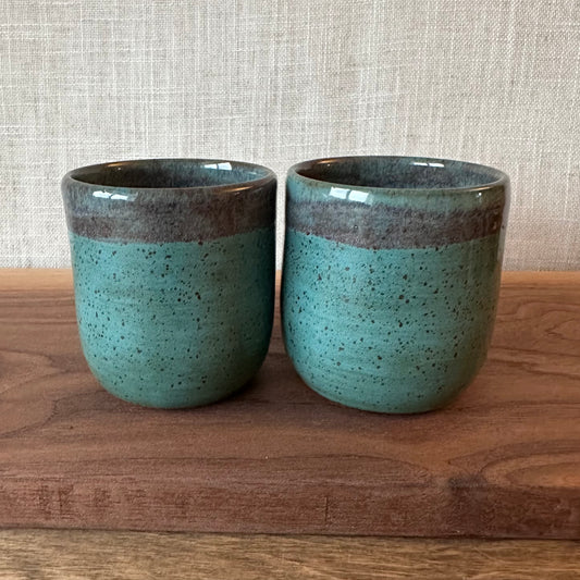 Two ceramic cups with a blue speckled glaze and brown rim on a wooden surface.