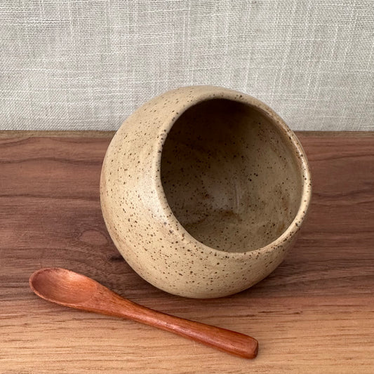 Ceramic bowl with speckled texture and wooden spoon on a wooden surface with a neutral background