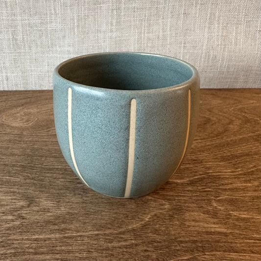 Blue ceramic cup with white stripes on a wooden surface with a textured gray wall background
