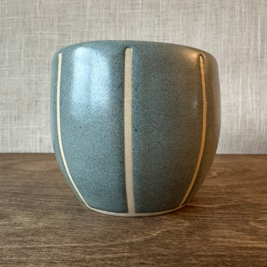 Blue ceramic vase with white stripe on a wooden surface and gray textured wall background