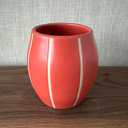 Red ceramic cup with white stripes on a wooden surface and gray textured background