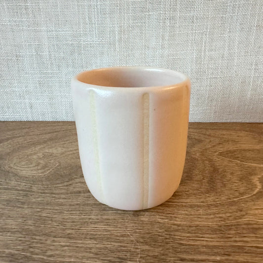 White ceramic cup with a beige rim on a wooden surface with a textured white background