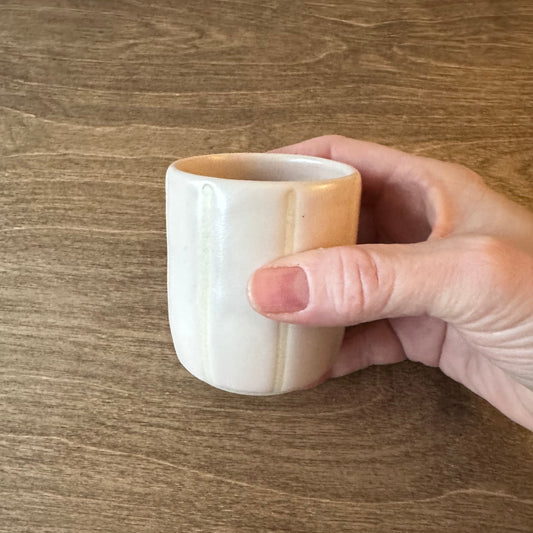 Hand holding a white ceramic cup with a wooden handle on a wooden surface