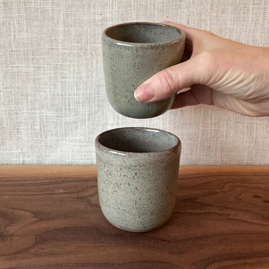Hand holding a ceramic cup with another cup on a wooden surface and textured wall background