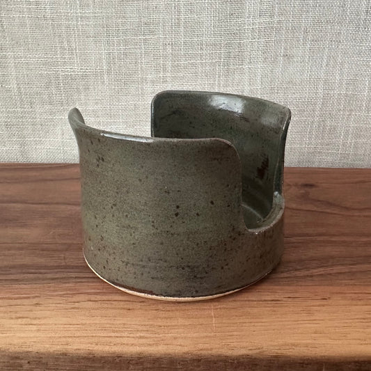 Green ceramic planter on a wooden surface with a textured gray wall background