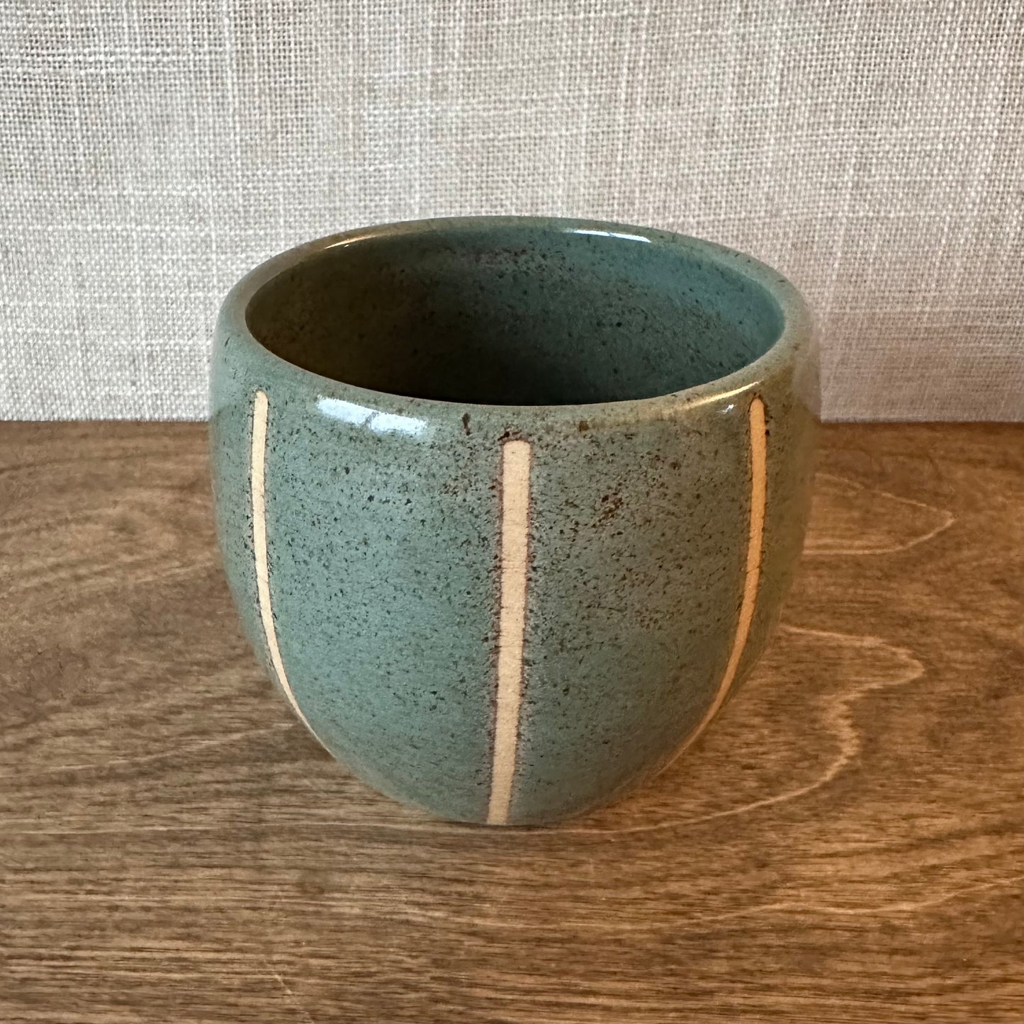 Green ceramic cup with white stripes on a wooden surface and textured wall background