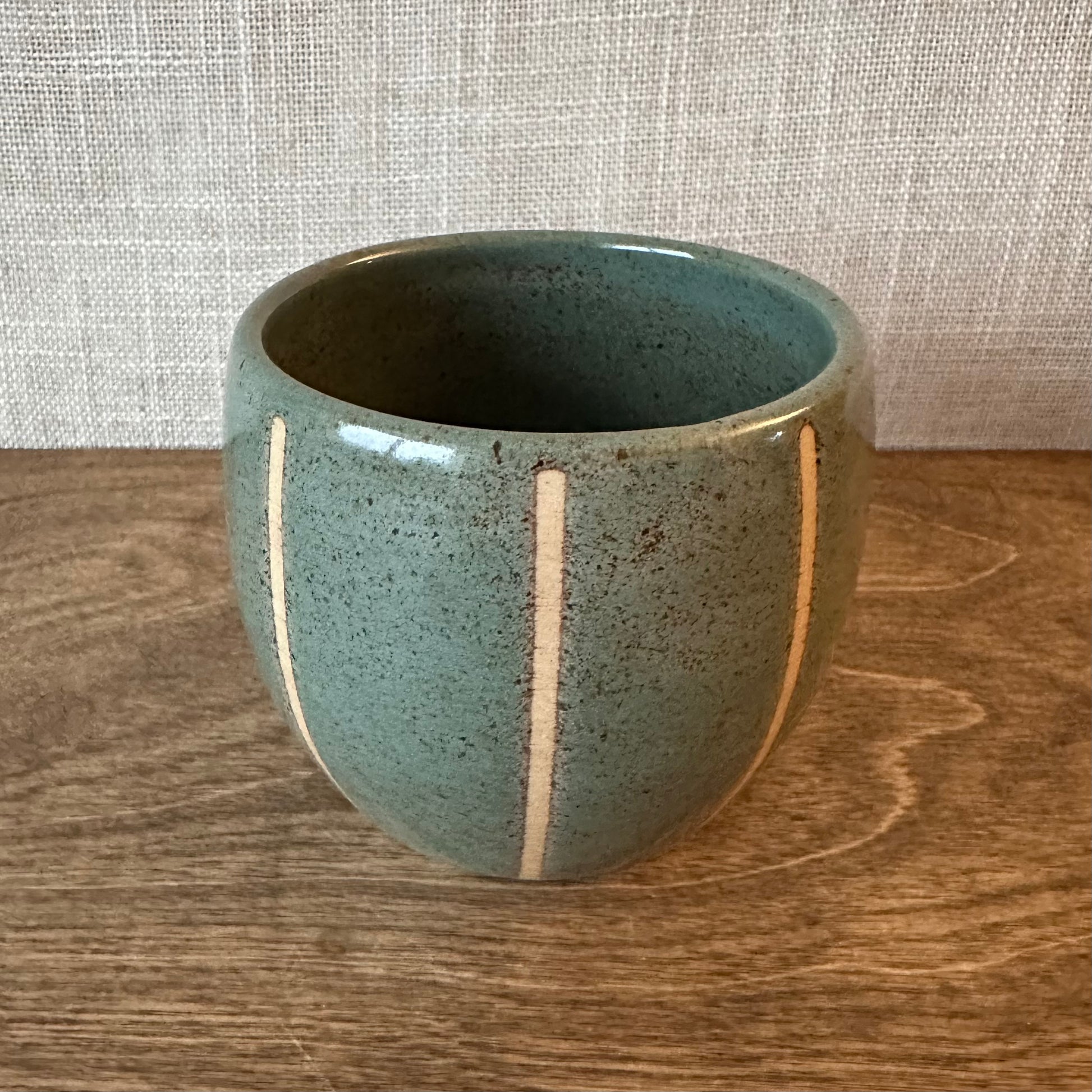 Green ceramic cup with white stripes on a wooden surface and textured wall background