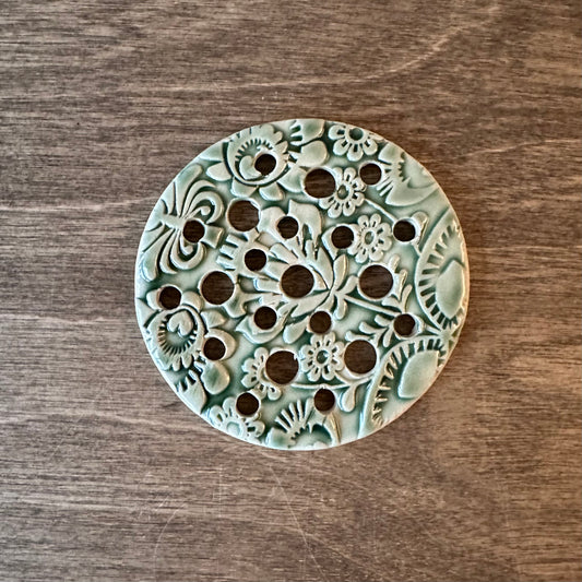 Decorative ceramic trivet with floral patterns on a wooden surface