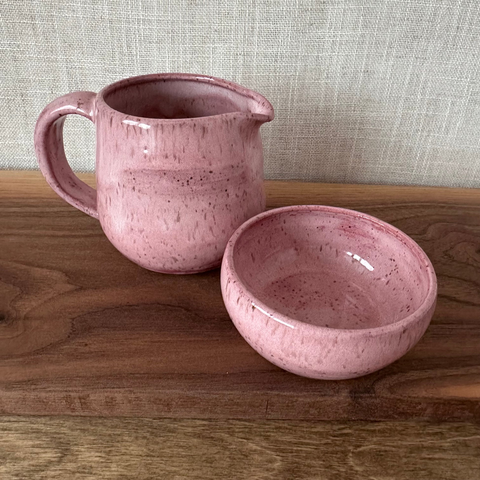 Pink ceramic pitcher and bowl on a wooden surface with a textured wall background