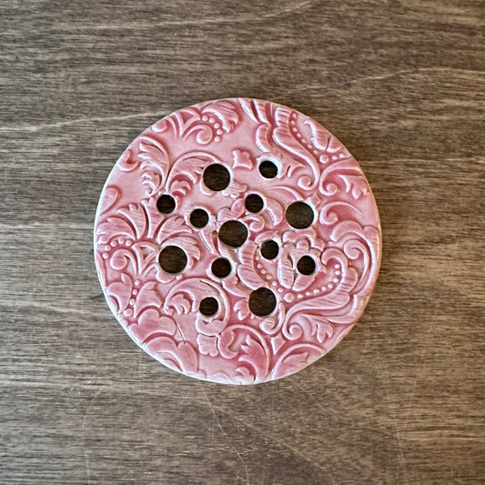 Pink ceramic trivet with decorative patterns on a wooden surface