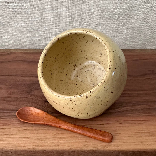 Speckled ceramic bowl with a wooden spoon on a wooden surface