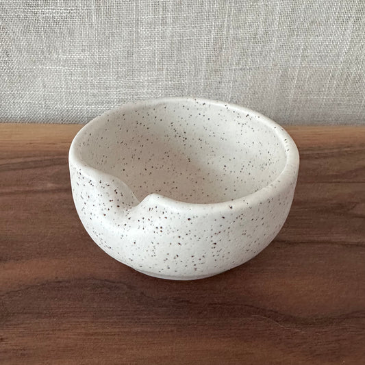 Speckled ceramic bowl on a wooden surface with a textured gray background