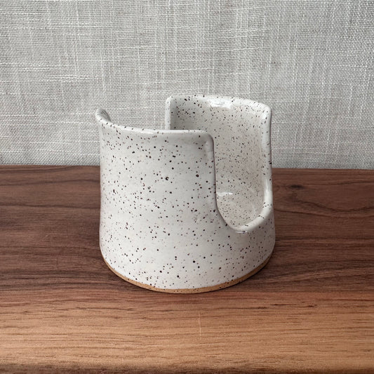 Speckled ceramic planter on a wooden surface with a textured gray wall background