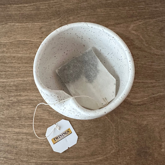 Tea bag in a speckled ceramic bowl on a wooden surface with a Twinings tea bag tag.
